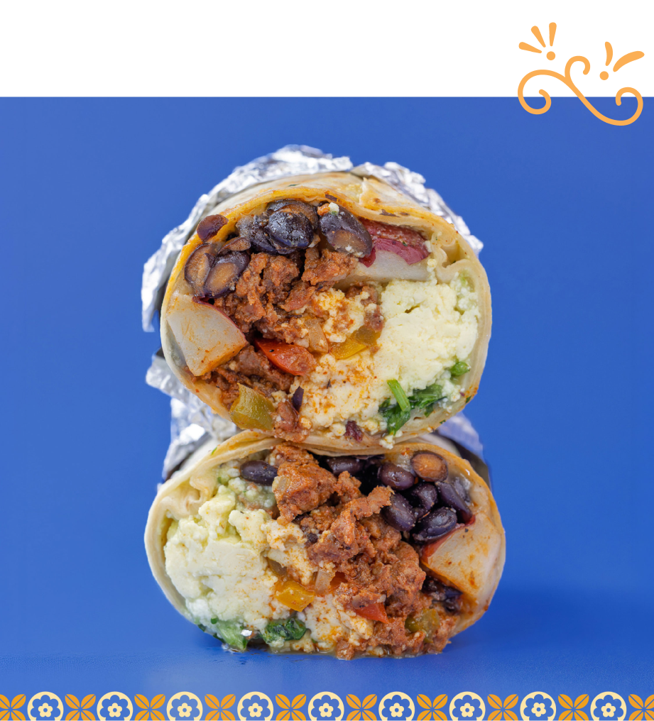 Breakfast burrito made with scrambled eggs, potatoes, black beans, fajita veggies, cilantro, queso fresco, and topped with guacamolio