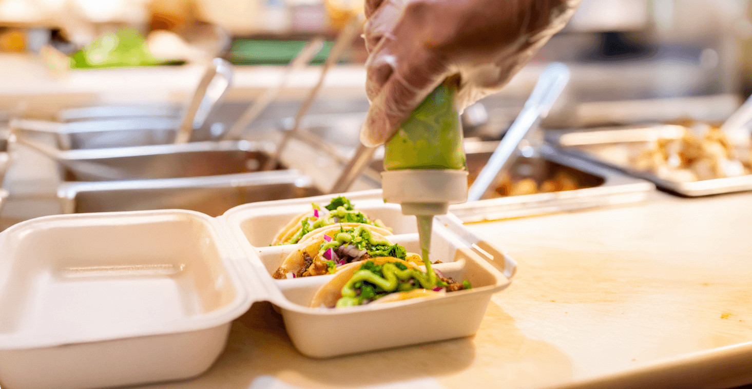 Image of avocado crema drizzled over tacos at take out counter