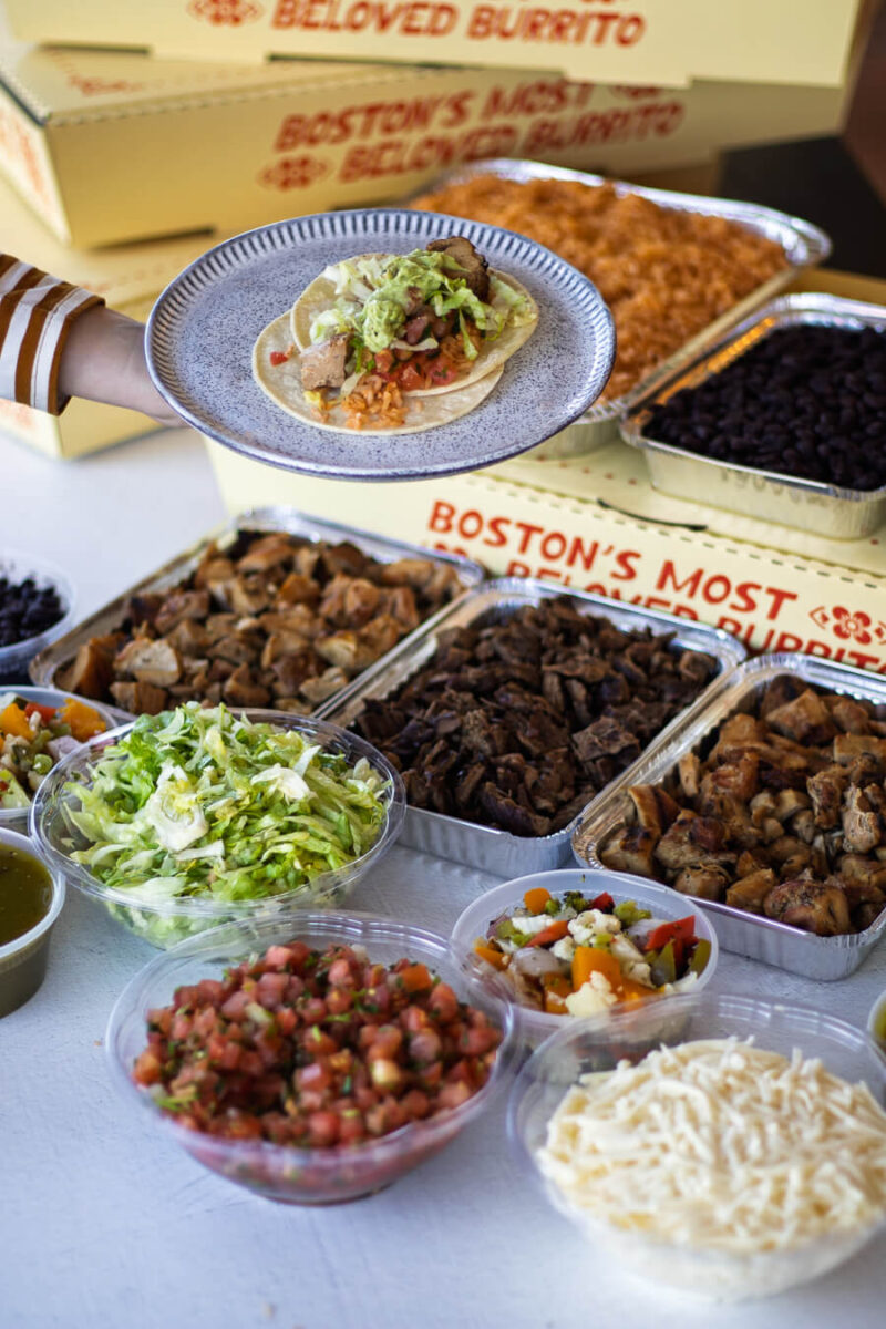 Anna's Taqueria catering setup with pre-made burritos, a make-your-own taco station, fresh ingredients, and Mexican soda